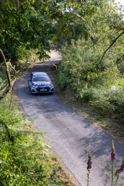 Bizimki, İspanya, 13 Haziran 2025: yüksek açı, dar, dolambaçlı bir yolda dolambaçlı, yemyeşil bitkilerle çevrili mavi bir rali aracının uzun yolu..
