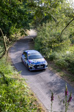 Ourense, İspanya, 13 Haziran 2025: yüksek açı, verimli yeşil yapraklar arasında dolambaçlı bir yolda ilerleyen mavi rali arabasının uzun görüntüsü..
