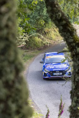 Bizimki, İspanya, 13 Haziran 2025: yüksek açı, ormandan geçen dolambaçlı bir yoldan geçen mavi rali aracının biraz belirsiz görüntüsü..