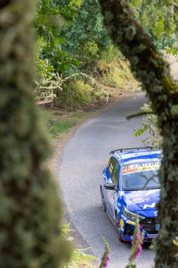 Ourense, İspanya, 13 Haziran 2025: yüksek açı, mavi rali arabasının ormandan geçen virajlı asfalt yolda keskin bir dönüş yapması uzak ihtimal..