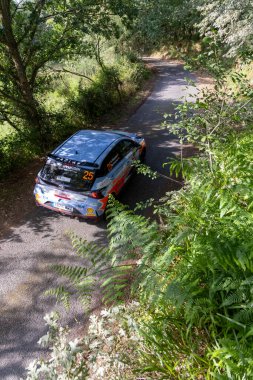 Ourense, İspanya, 13 Haziran 2025: yüksek açı, dar bir yolda park etmiş bir ralli aracının tam görüntüsü çevre yapraklarla kısmen gizlenmiş..