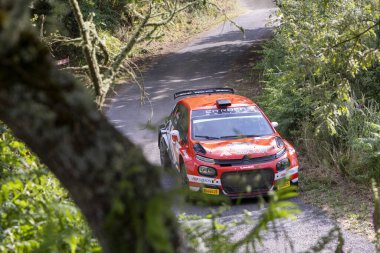 Ourense, İspanya, 13 Haziran 2025: Görüntüde yoğun bir ormanın içinden geçen dar, toprak bir yolda hareket eden kırmızı bir ralli arabası görülüyor.