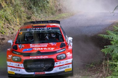 Ourense, İspanya, 13 Haziran 2025: Dar bir orman yolunda keskin bir dönüş yapan kırmızı ralli arabasının yüksek açılı, dinamik bir görüntüsü.