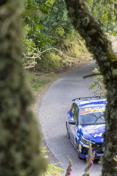 Ourense, İspanya, 13 Haziran 2025: yüksek açı, mavi rali arabasının ormandan geçen virajlı asfalt yolda keskin bir dönüş yapması uzak ihtimal..
