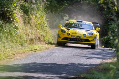 Ourense, İspanya, 13 Haziran 2025: Görüntü ön planda keskin bir şekilde odaklanmış çakıl yolunda hareketli canlı sarı bir rali arabası sergiliyor.