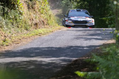 Ourense, İspanya, 13 Haziran 2025: Görüntü, sağa doğru keskin virajlı dar bir asfalt yolda hareket eden bir ralli arabasını gösteriyor