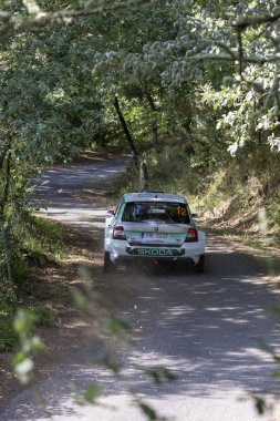 Ourense, İspanya, 13 Haziran 2025: Görüntü, yemyeşil bir ormanda dolambaçlı toprak bir yolda ilerleyen beyaz bir rali aracının dikiz görüntüsünü gösteriyor..