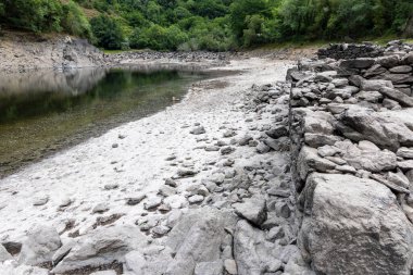 Görüntü yüksek açılı, düşük su seviyeli bir nehir görüntüsü veriyor. Açığa çıkan nehir yatağı ağırlıklı olarak çeşitli boylarda açık gri ve koyu gri taşlardan oluşur.,