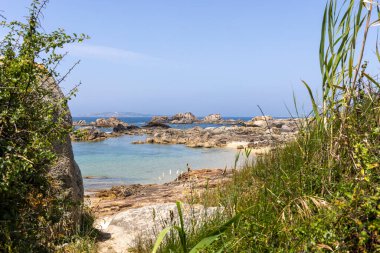 Kayalık bir kıyı şeridi ve suya giden küçük bir patika. Su sakin ve mavi.