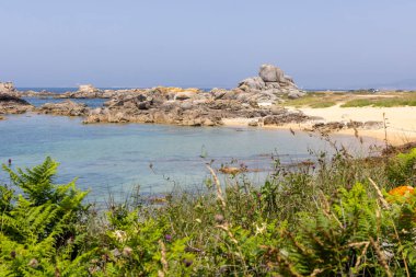 Kayalık bir kıyı şeridi ve suya giden küçük bir patika. Su sakin ve mavi.