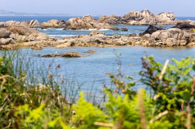 Kayalık bir kıyı şeridi ve suya giden küçük bir patika. Su sakin ve mavi.
