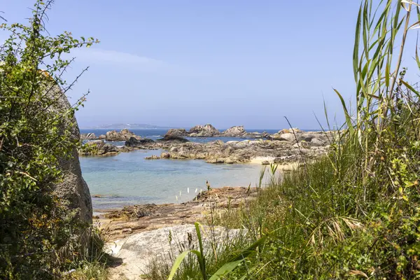 Kayalık bir kıyı şeridi ve suya giden küçük bir patika. Su sakin ve mavi.