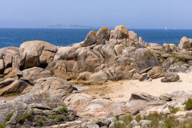 Arka planda büyük bir su kütlesi olan kayalık bir sahil. Kayalar sahile dağılmış, engebeli ve doğal bir manzara yaratıyorlar. Huzur ve yalnızlık kavramı