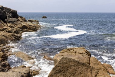 Okyanus sakin ve gökyüzü açık. Kıyı şeridine dağılmış kayalar güzel ve huzurlu bir manzara yaratıyor.