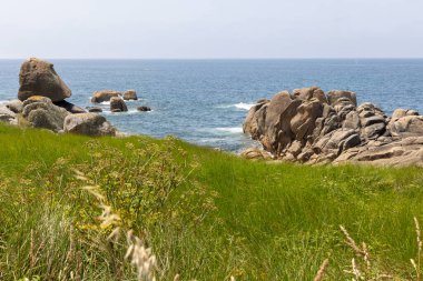 Bir yelkenli okyanusta kayaların yanında seyrediyor. Gökyüzü açık ve su sakin.