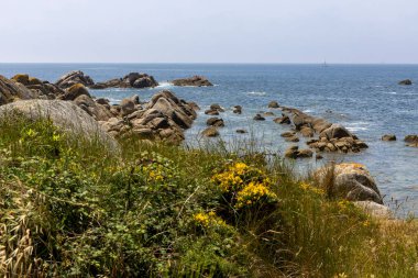 Suda küçük bir teknesi olan kayalık bir kıyı şeridi. Gökyüzü açık ve okyanus sakin