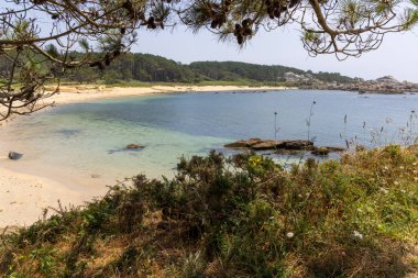 Arka planda su bulunan bir plaj. Su berrak ve sakin. Kumsal kumlu ve suda bazı kayalar var. Huzurlu ve huzurlu bir sahne.