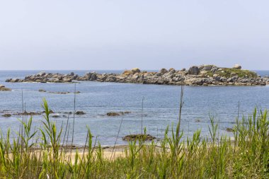 Arka planda su bulunan bir plaj. Su berrak ve sakin. Kumsal kumlu ve suda bazı kayalar var. Huzurlu ve huzurlu bir sahne.