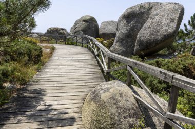 Her iki tarafında taş duvar olan ahşap bir geçit. Geçit ağaçlar ve kayalarla çevrili.