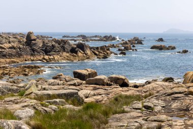 Önünde büyük bir kaya olan kayalık bir kıyı şeridi. Kayalar kıyı şeridi boyunca dağılmış ve su sakin. Sahnenin huzurlu ve huzurlu bir havası var.