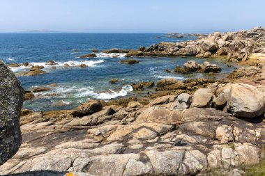 Suda küçük bir teknesi olan kayalık bir kıyı şeridi. Gökyüzü açık ve okyanus sakin