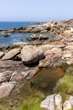 Suda küçük bir teknesi olan kayalık bir kıyı şeridi. Gökyüzü açık ve okyanus sakin