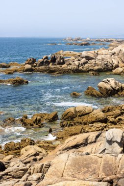 Suda küçük bir teknesi olan kayalık bir kıyı şeridi. Gökyüzü açık ve okyanus sakin