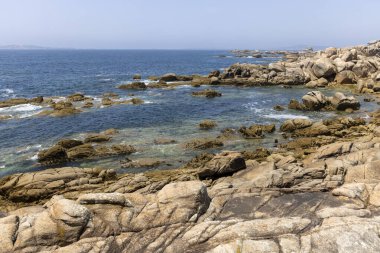 Suda küçük bir teknesi olan kayalık bir kıyı şeridi. Gökyüzü açık ve okyanus sakin