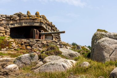 Üstünde silah olan büyük taştan bir bina. Binanın etrafı kayalarla çevrili ve taş bir duvarı var. Sahne güç ve korumadır.