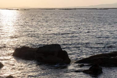 Okyanus sakin ve güneş batıyor. Su koyu mavi bir renktir ve gökyüzü açık mavi bir renktir.