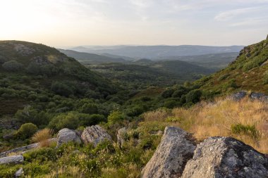 Altında yemyeşil bir vadi olan bir dağ sırası. Gökyüzü mavi ve beyazın karışımı, birkaç bulut dağılmış. Sahne huzurlu ve sakin, dağlarla birlikte.
