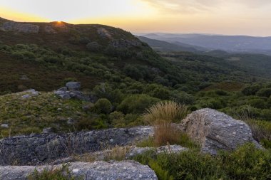 Altında yemyeşil bir vadi olan bir dağ sırası. Gökyüzü mavi ve beyazın karışımı, birkaç bulut dağılmış. Sahne huzurlu ve sakin, dağlarla birlikte.