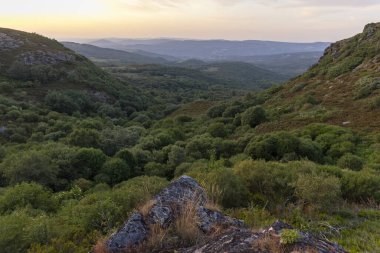 Altında yemyeşil bir vadi olan bir dağ sırası. Gökyüzü mavi ve beyazın karışımı, birkaç bulut dağılmış. Sahne huzurlu ve sakin, dağlarla birlikte.