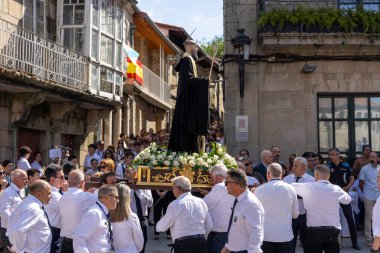 Allariz, İspanya, 13 Temmuz 2025: Büyük bir heykel taşıyan bir grup insan. İnsanlar siyah ve beyaz giyinmiş ve heykel çiçeklerle çevrili..