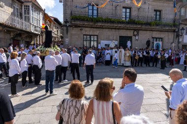 Allariz, İspanya, 13 Temmuz 2025: Büyük bir heykel taşıyan bir grup insan. İnsanlar siyah ve beyaz giyinmiş ve heykel çiçeklerle çevrili..
