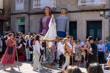 Allariz, İspanya, 13 Temmuz 2025: Büyük bir heykel taşıyan bir grup insan. İnsanlar siyah ve beyaz giyinmiş ve heykel çiçeklerle çevrili..