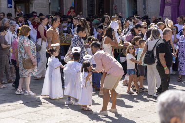 Allariz, İspanya, 13 Temmuz 2025: Bir grup insan dışarıda duruyor, bazıları beyaz elbiseler giyiyor. Bir adam kucağında bir çocuk tutuyor.