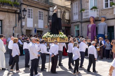 Allariz, İspanya, 13 Temmuz 2025: Büyük bir heykel taşıyan bir grup insan. İnsanlar siyah ve beyaz giyinmiş ve heykel çiçeklerle çevrili..