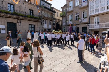 Allariz, İspanya, 13 Temmuz 2025: Büyük bir heykel taşıyan bir grup insan. İnsanlar siyah ve beyaz giyinmiş ve heykel çiçeklerle çevrili..