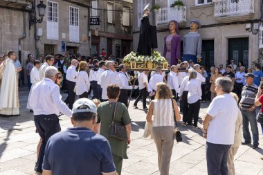 Allariz, İspanya, 13 Temmuz 2025: Büyük bir heykel taşıyan bir grup insan. İnsanlar siyah ve beyaz giyinmiş ve heykel çiçeklerle çevrili..