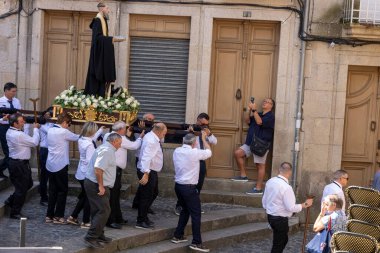 Allariz, İspanya, 13 Temmuz 2025: Büyük bir heykel taşıyan bir grup insan. İnsanlar siyah ve beyaz giyinmiş ve heykel çiçeklerle çevrili..