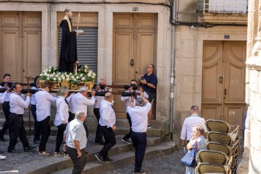 Allariz, İspanya, 13 Temmuz 2025: Büyük bir heykel taşıyan bir grup insan. İnsanlar siyah ve beyaz giyinmiş ve heykel çiçeklerle çevrili..