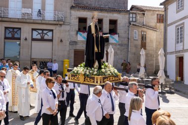 Allariz, İspanya, 13 Temmuz 2025: Büyük bir heykel taşıyan bir grup insan. İnsanlar siyah ve beyaz giyinmiş ve heykel çiçeklerle çevrili..