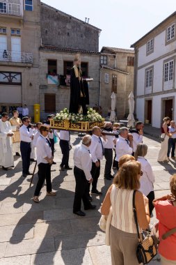 Allariz, İspanya, 13 Temmuz 2025: Büyük bir heykel taşıyan bir grup insan. İnsanlar siyah ve beyaz giyinmiş ve heykel çiçeklerle çevrili..