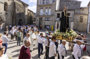 Allariz, İspanya, 13 Temmuz 2025: Büyük bir heykel taşıyan bir grup insan. İnsanlar siyah ve beyaz giyinmiş ve heykel çiçeklerle çevrili..