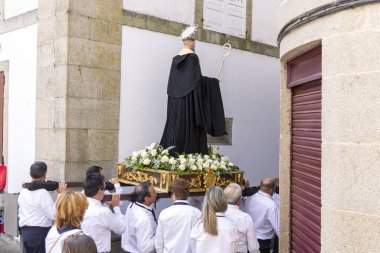 Allariz, İspanya, 13 Temmuz 2025: Büyük bir heykel taşıyan bir grup insan. İnsanlar siyah ve beyaz giyinmiş ve heykel çiçeklerle çevrili..