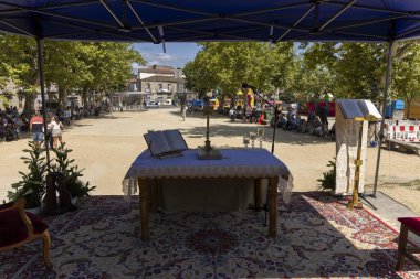 Allariz, İspanya, 13 Temmuz 2025: Altında masa ve sandalyeler olan bir parkta mavi bir çadır kuruldu. Masanın üzerinde bir kitap ve masanın üzerinde de bir haç var..