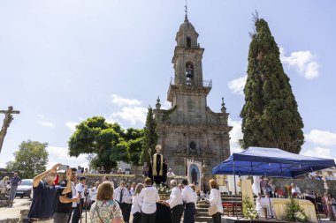 Allariz, İspanya, 13 Temmuz 2025: Siyah cübbeli bir adam asasını tutuyor ve etrafı insanlarla çevrili. Sahne, çan kulesi olan büyük bir kilisenin önünde geçiyor. Atmosfer dinsel ve ağırbaşlı görünüyor.