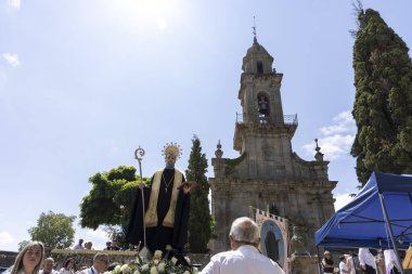 Allariz, İspanya, 13 Temmuz 2025: Siyah cübbeli bir adam asasını tutuyor ve etrafı insanlarla çevrili. Sahne, çan kulesi olan büyük bir kilisenin önünde geçiyor. Atmosfer dinsel ve ağırbaşlı görünüyor.