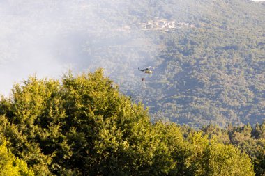 Allariz, İspanya, 16 Temmuz 2025: Arka planda yangın olan bir orman üzerinde bir helikopter uçuyor. Helikopter yangını söndürüyor.